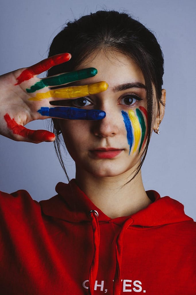 woman in red hoodie jacket with blue yellow and green paint on face
